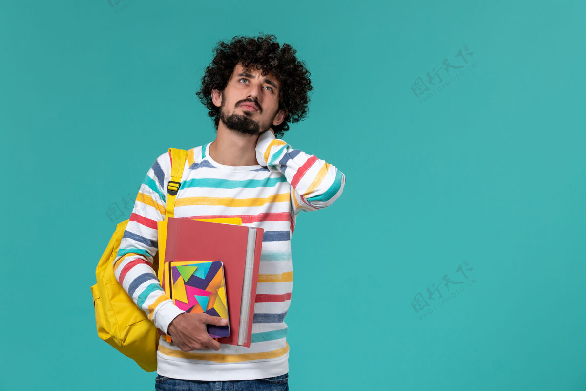 衬衫前视图中的男学生穿着彩色条纹衬衫 背着黄色的背包 手里拿着文件和复印件 蓝色的墙上有脖子学院条纹喜剧演员