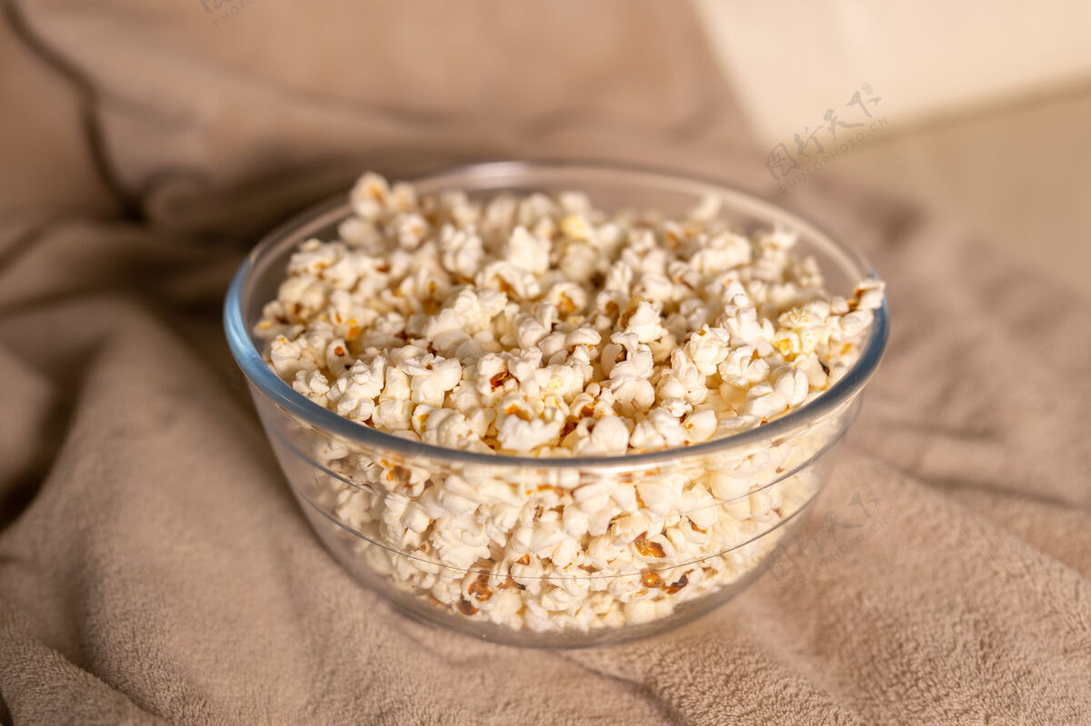 娱乐一碗爆米花在米色沙发上看电影零食和不健康的垃圾食品的概念美味电影室内