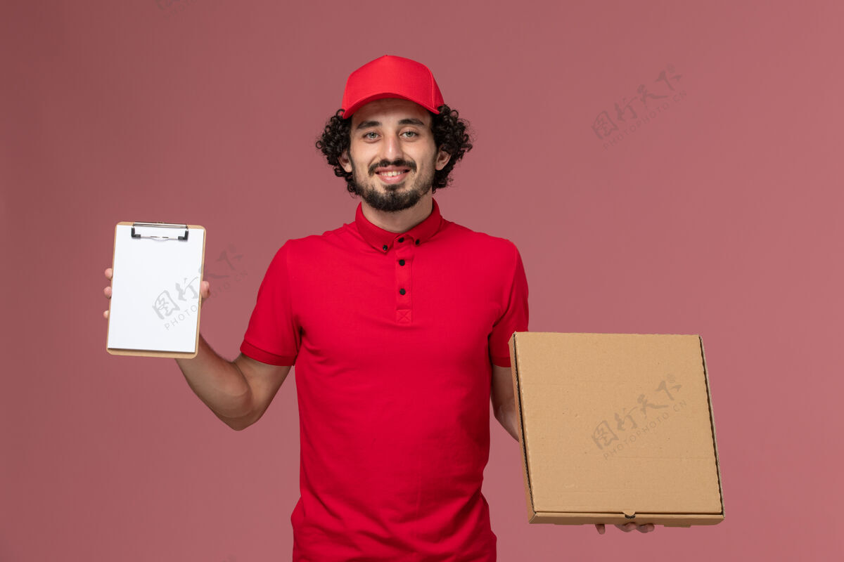 前面正面图穿着红色衬衫和披风的男信使拿着送食物的盒子和粉色墙上的记事本帽子工人男