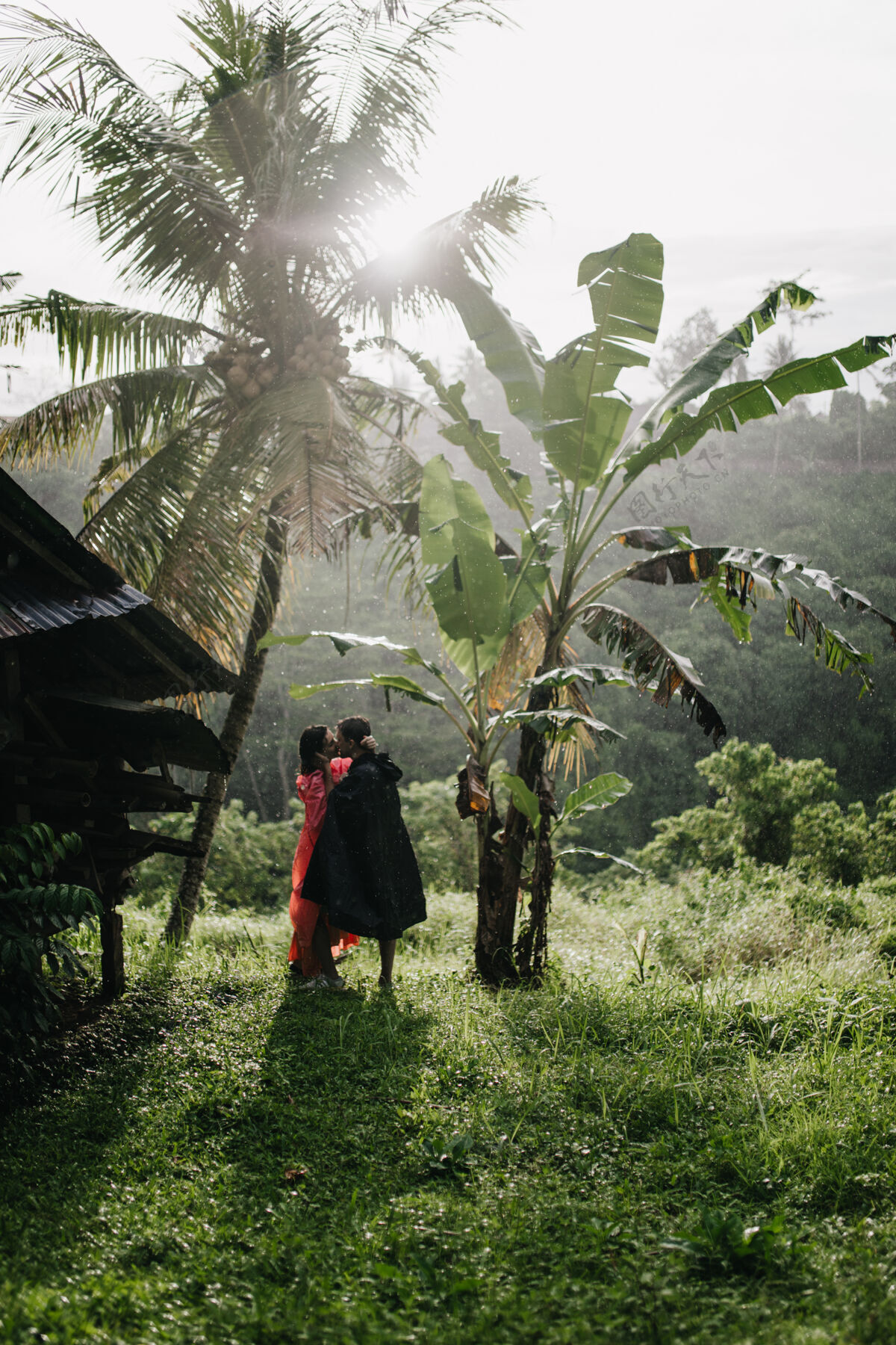 休闲穿着黑色雨衣的旅行者在异国情调的森林里亲吻女人的全长肖像在雨林里度过时光的幸福夫妻雨林风景夫妻